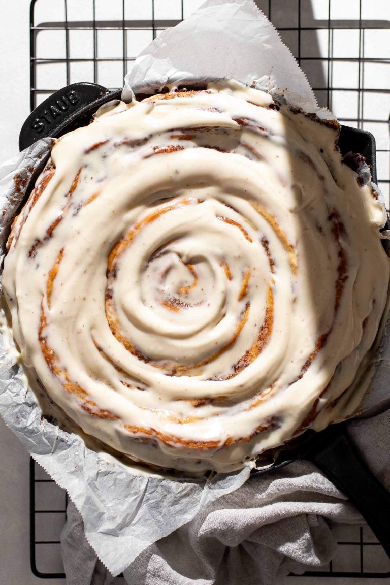 iced giant cinnamon roll cake in pan set onto wire rack