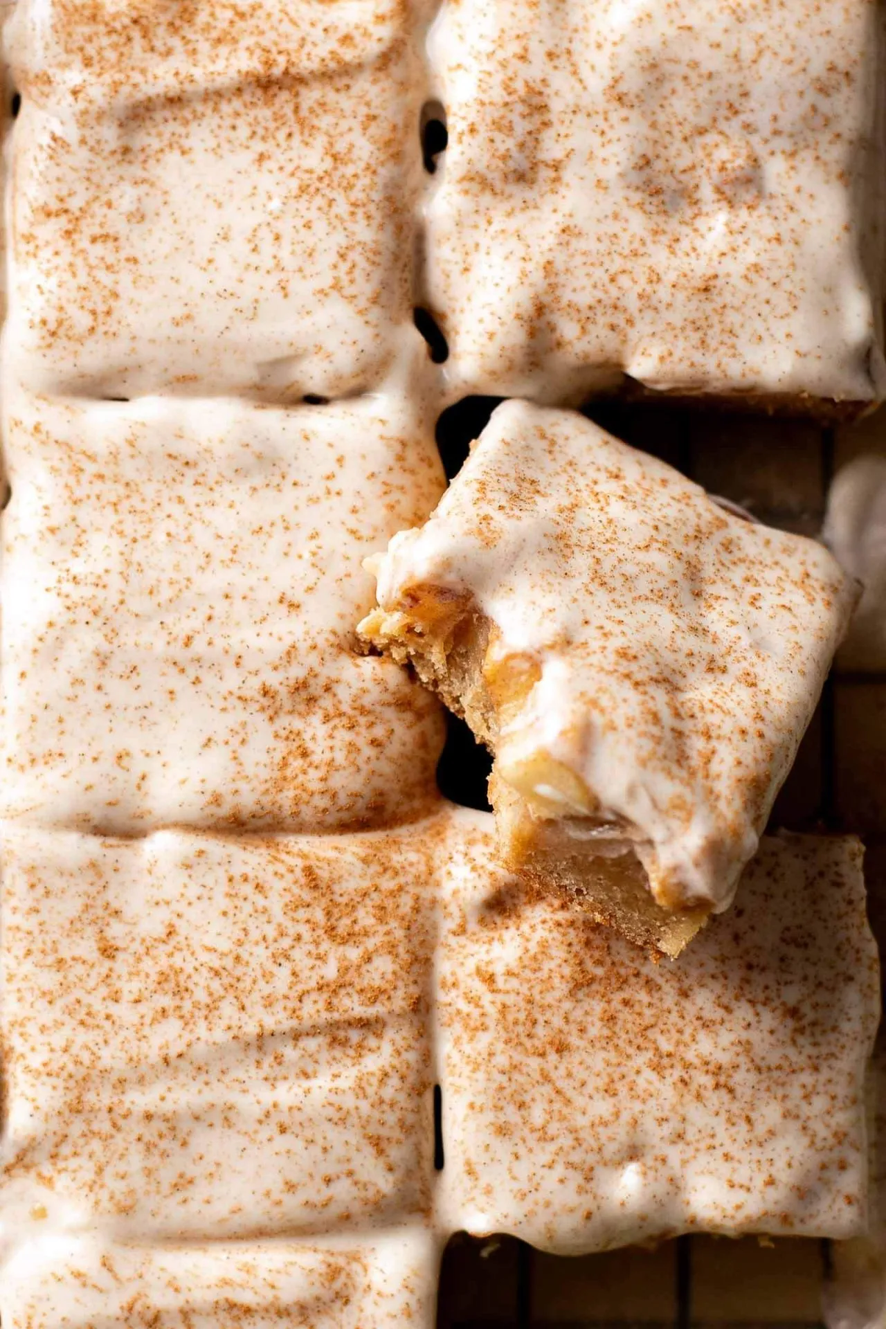 iced brown butter apple blondies on parchment lined wire rack with one missing bite overhead image