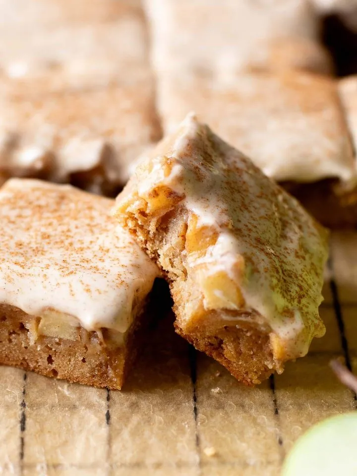 iced brown butter apple blondies on parchment lined wire rack close up of blondie with bite missing
