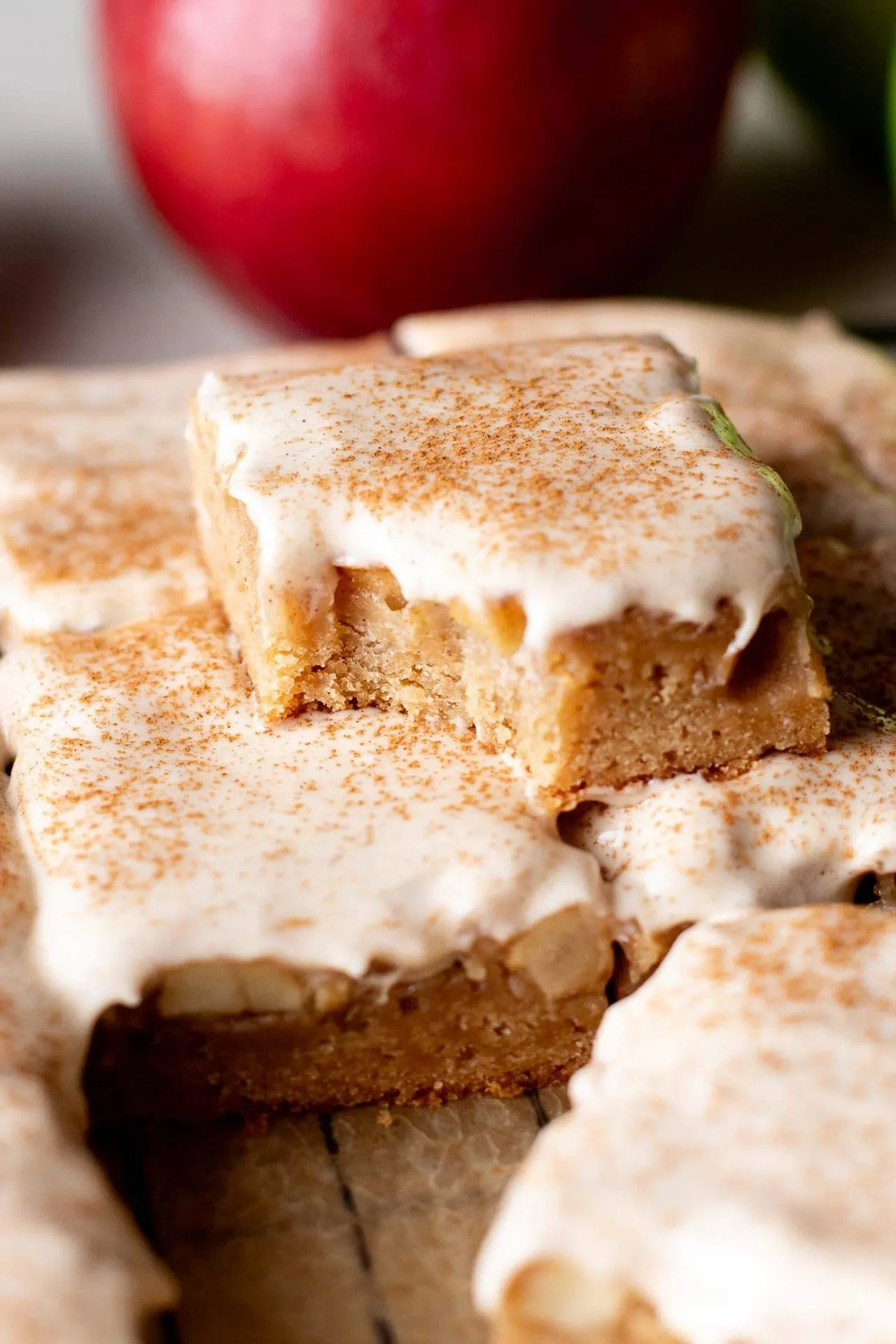 iced brown butter apple blondies on parchment lined wire rack with one missing bite head on image