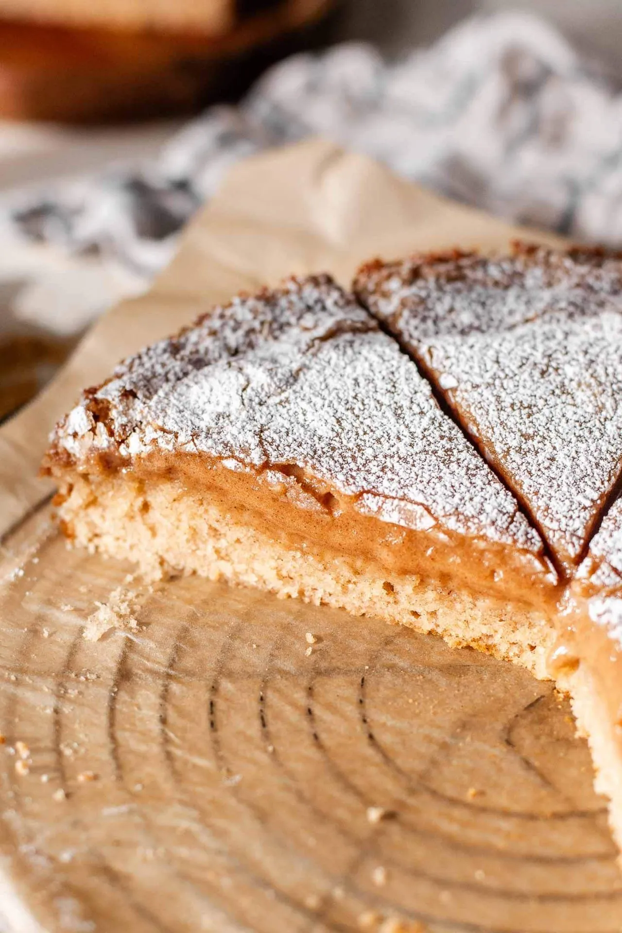 sliced cinnamon roll ooey gooey butter cake topped with dusting of powdered sugar on parchment paper (6)